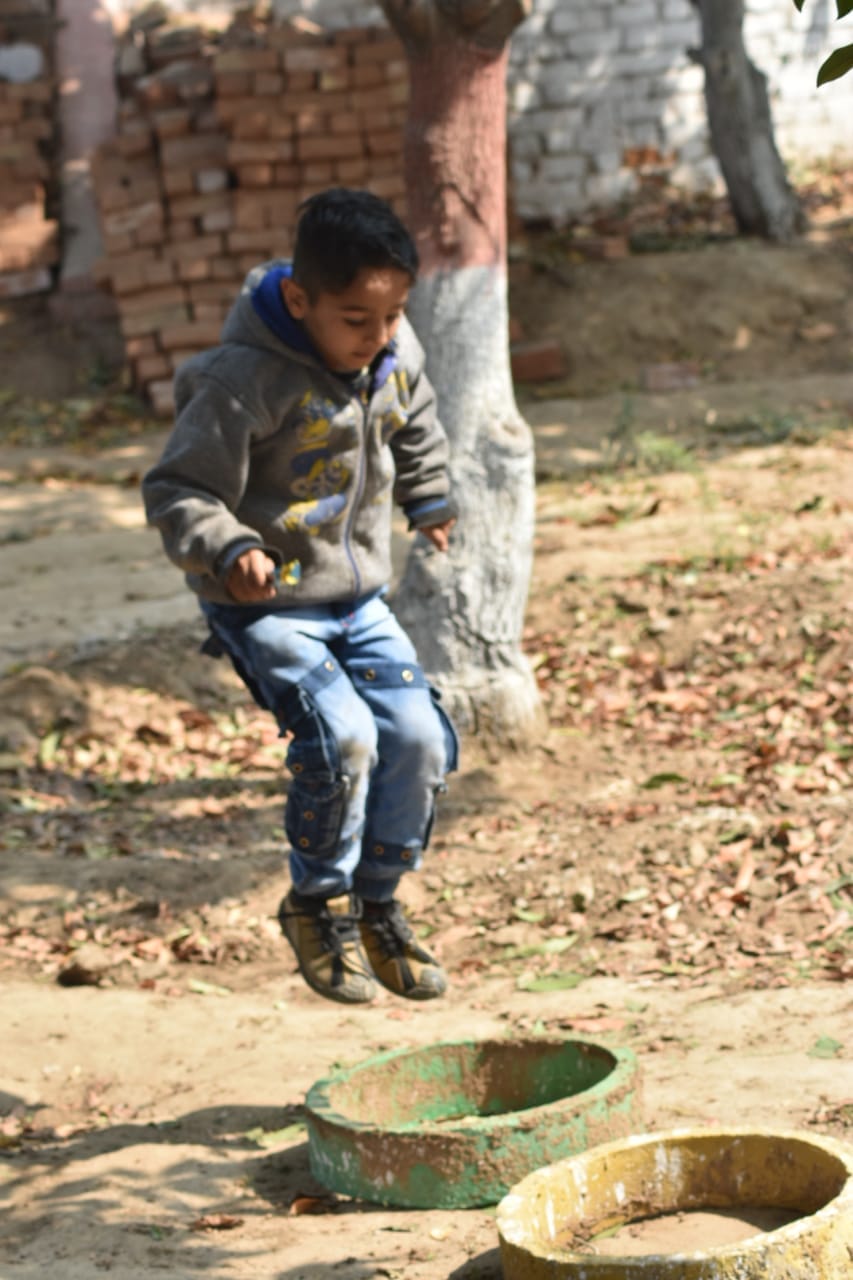 Young boy outdoors, mid-movement, with handmade/open outdoor play equipment in foreground