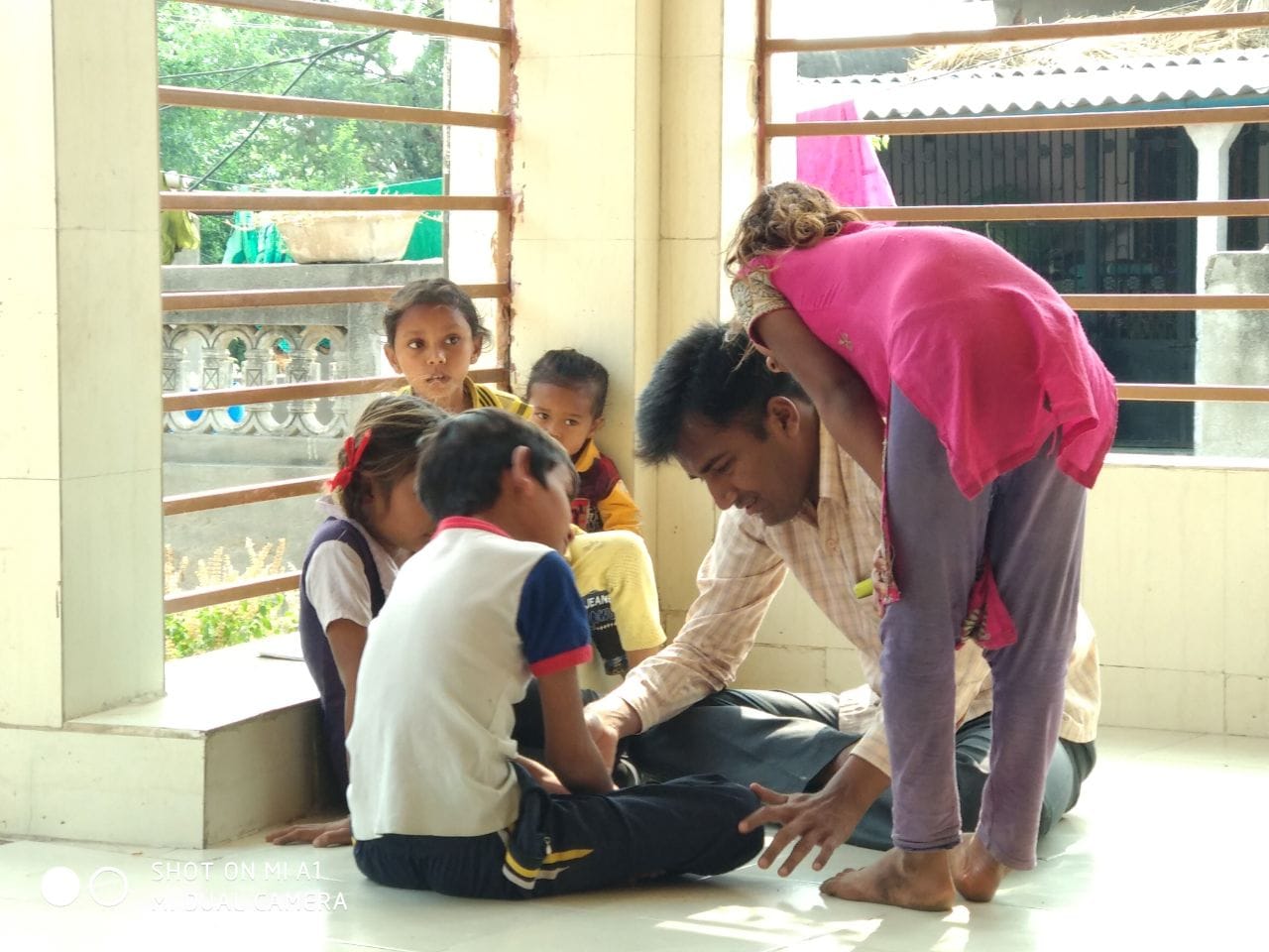 Volunteer and children engaged in a practical physical activity inside a community space; appears to involve helping/working around a participant