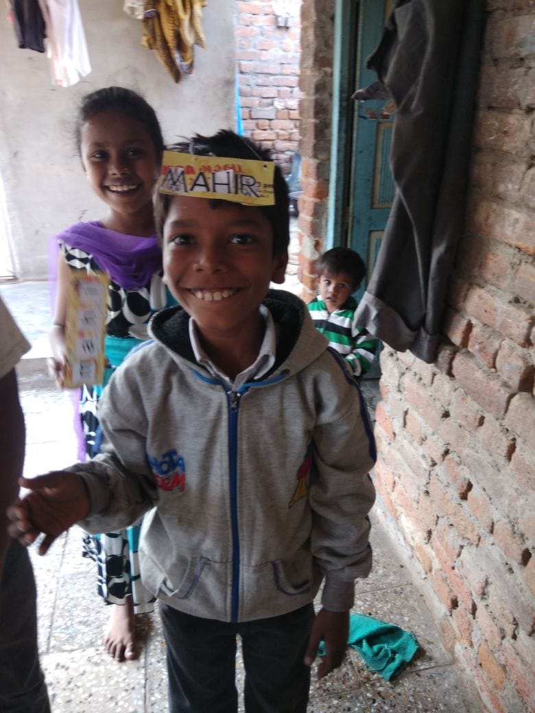 Child smiling and proudly displaying a handmade learning/name card; village home setting