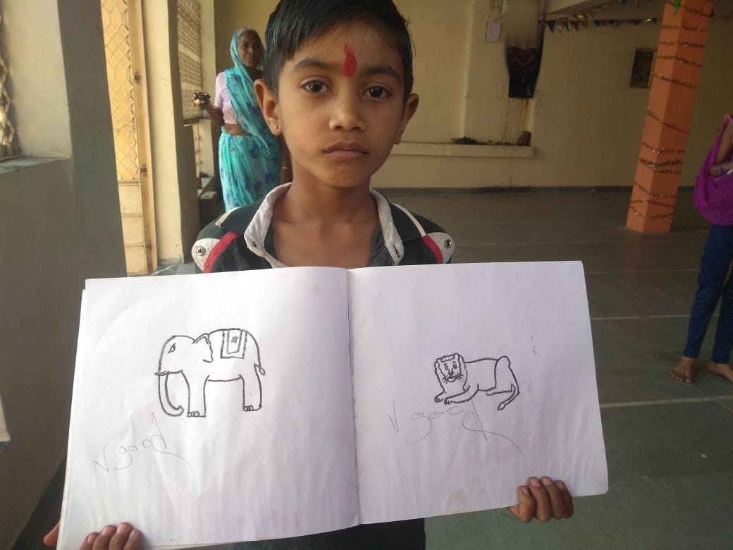 Boy holding open notebook with his drawings of an elephant and lion
