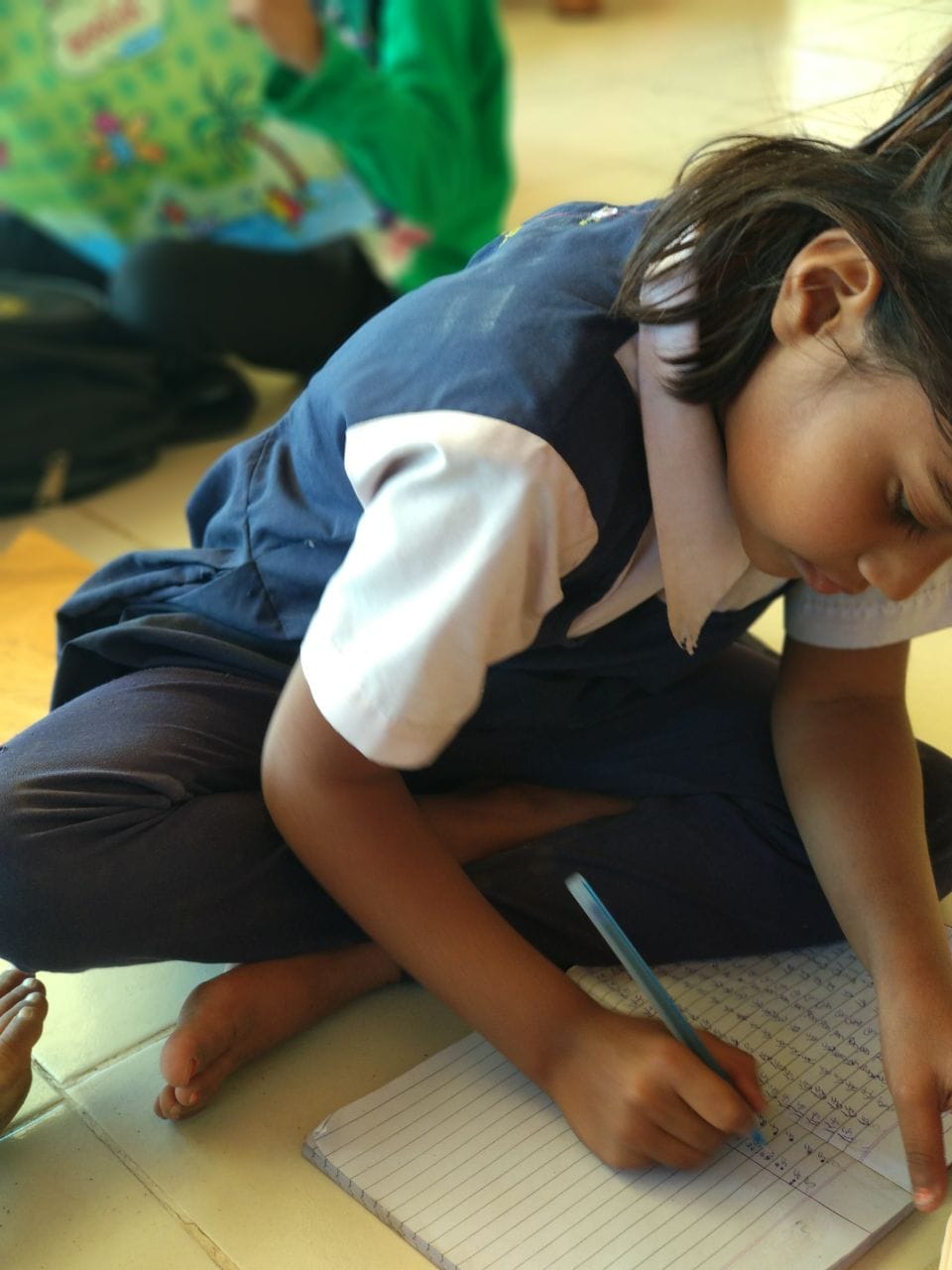 Girl intensely writing in notebook while seated on floor