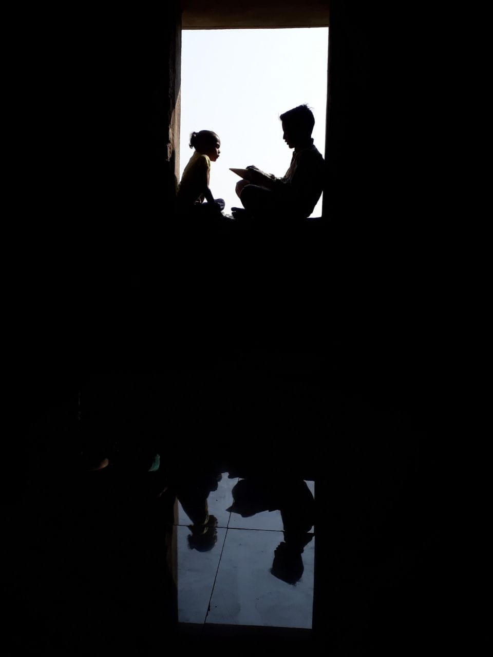 Silhouettes of an older participant and a child reading together in a doorway.