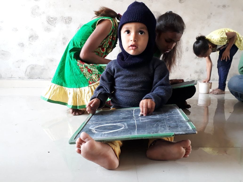Very young child using a slate while other children work in the background