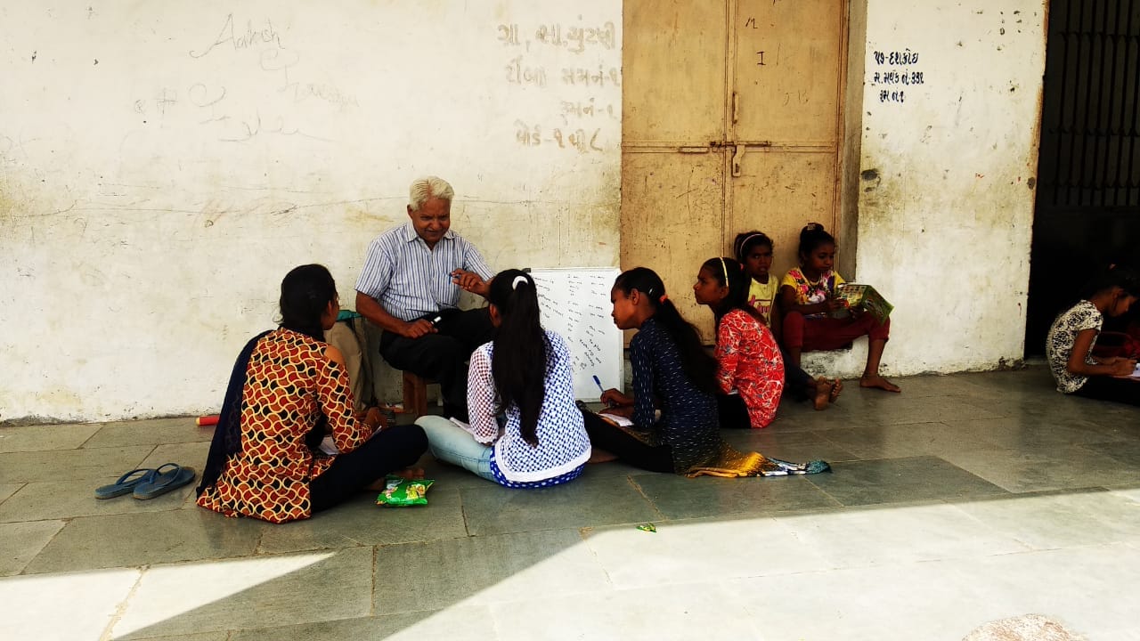 An older volunteer shares learning material with a small group of children in a village setting.