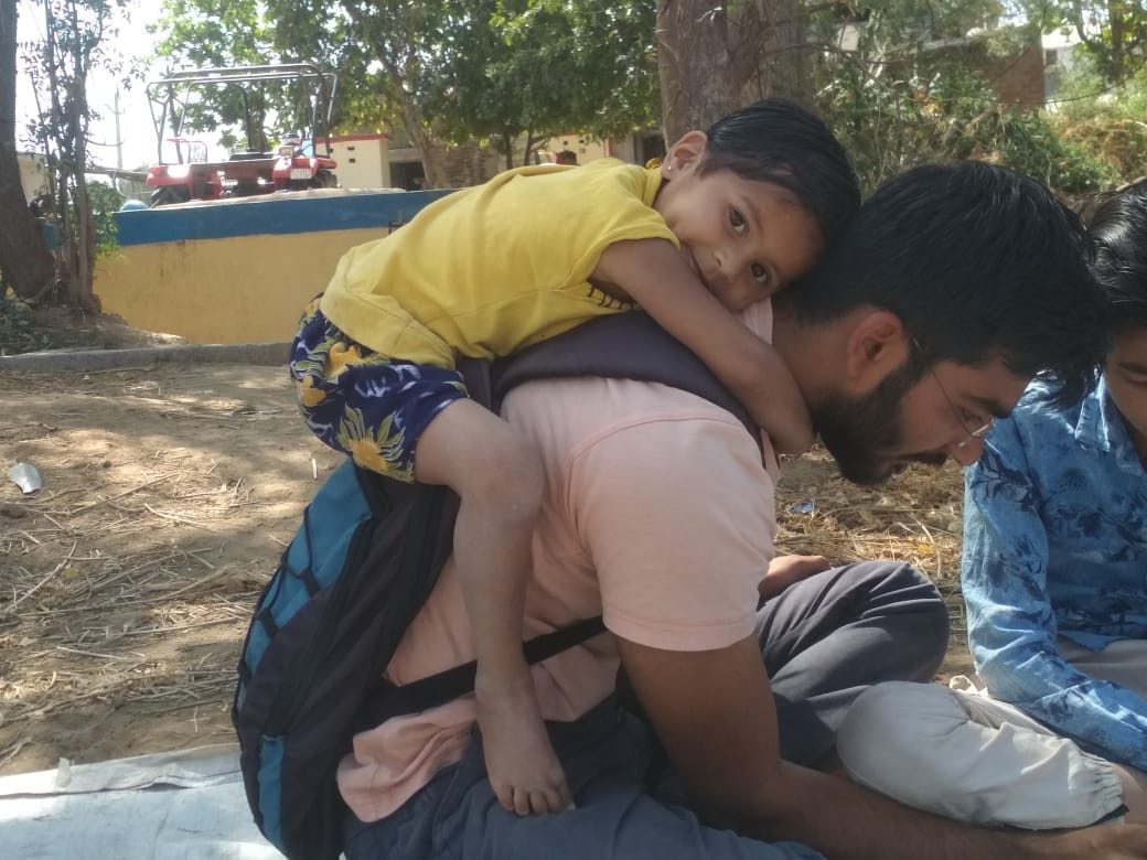 Volunteer carrying a young child on his back while another participant works nearby