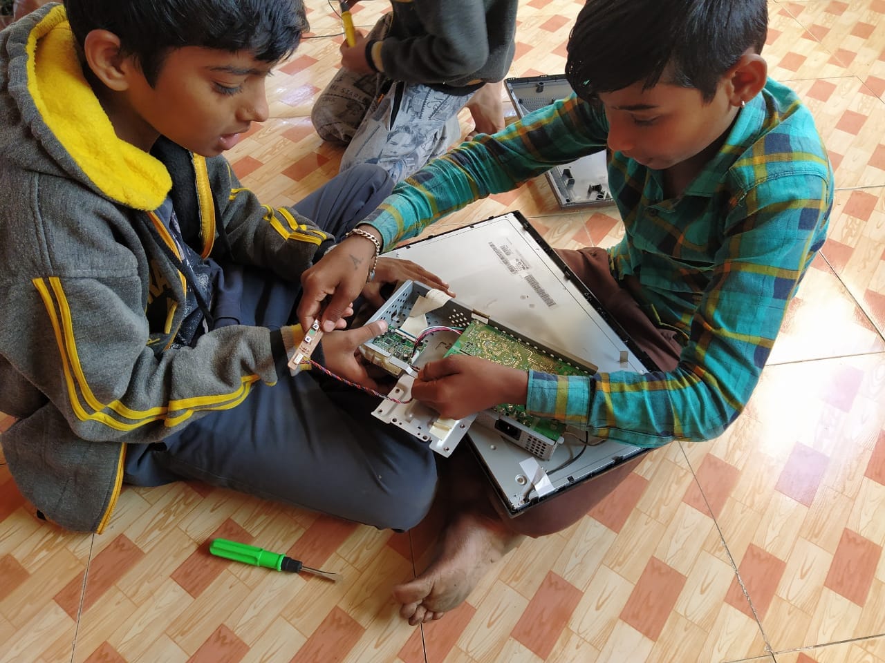 Two children examine the circuit board inside an opened computer monitor.