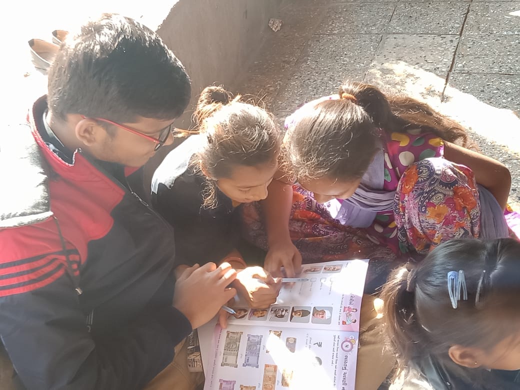 Children studying an illustrated/financial-learning worksheet together outdoors