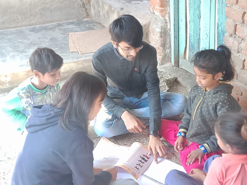 Young volunteer sitting with several children around a book/workbook