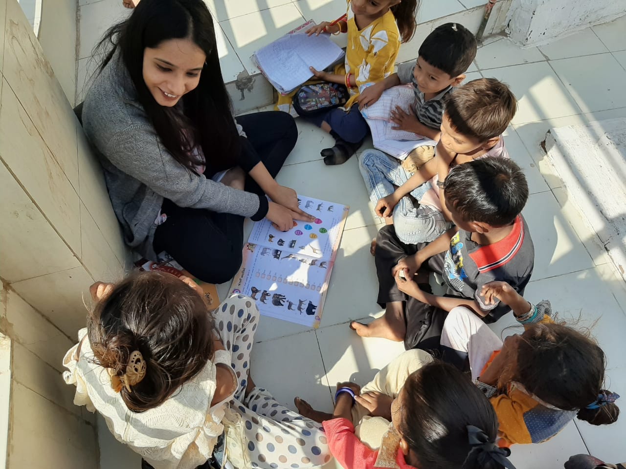 Young woman sitting with children and teaching from illustrated material